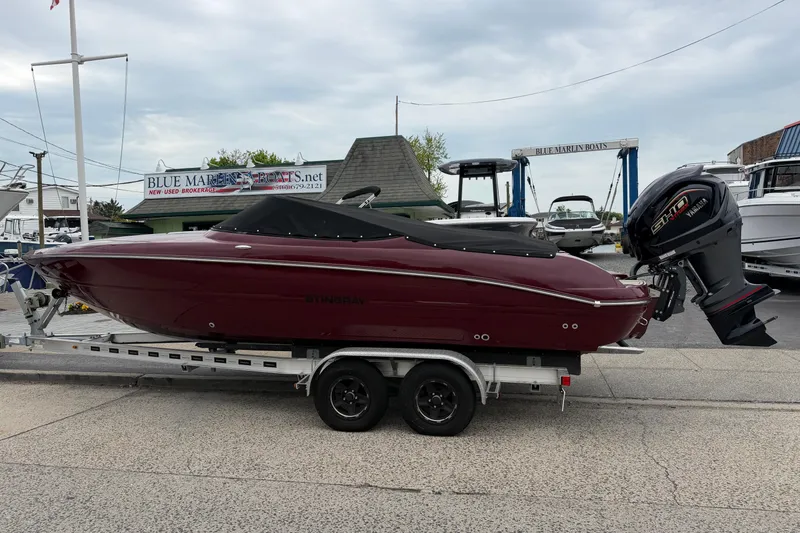 The Image of 2026 Stingray 23 OCX boat on trailer, maroon color, Yamaha outboard motor, at marina. - 1
