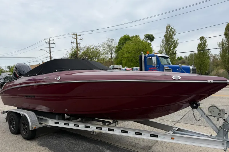 Slide: The Image of 2026 Stingray 23 OCX boat on trailer, maroon color, parked outdoors. - 2