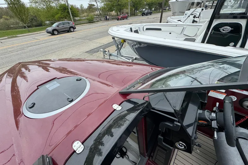 Slide: The Image of 2026 Stingray 23 OCX boat with maroon deck, parked near a road. - 28
