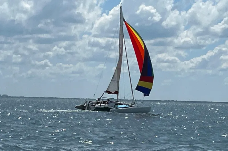 The Image of Sailing Corsair F 27 trimaran with colorful spinnaker on open water, under a partly cloudy sky. - 1