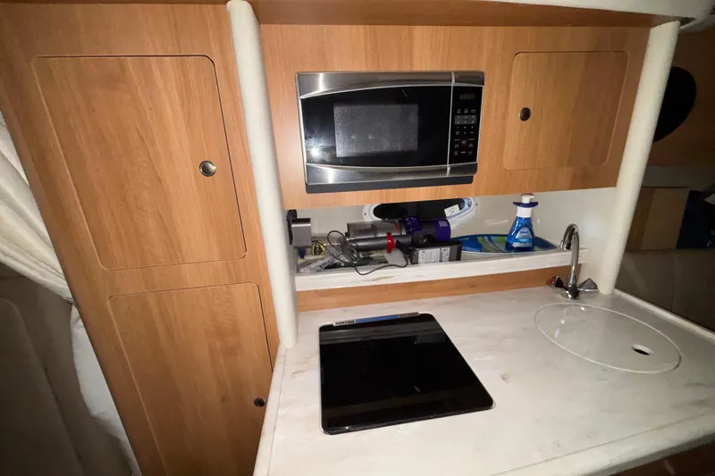 Slide: The Image of 2014 Rinker 290 Express Cruiser kitchen with microwave, sink, and storage cabinets. - 40