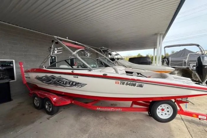 The Image of 2005 MasterCraft XStar boat on red trailer under a covered area. - 0