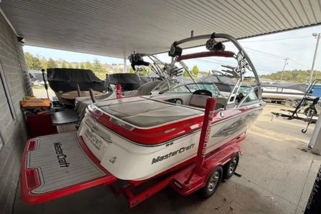 Slide: The Image of 2005 MasterCraft XStar boat with red accents on a trailer, parked under a canopy. - 2
