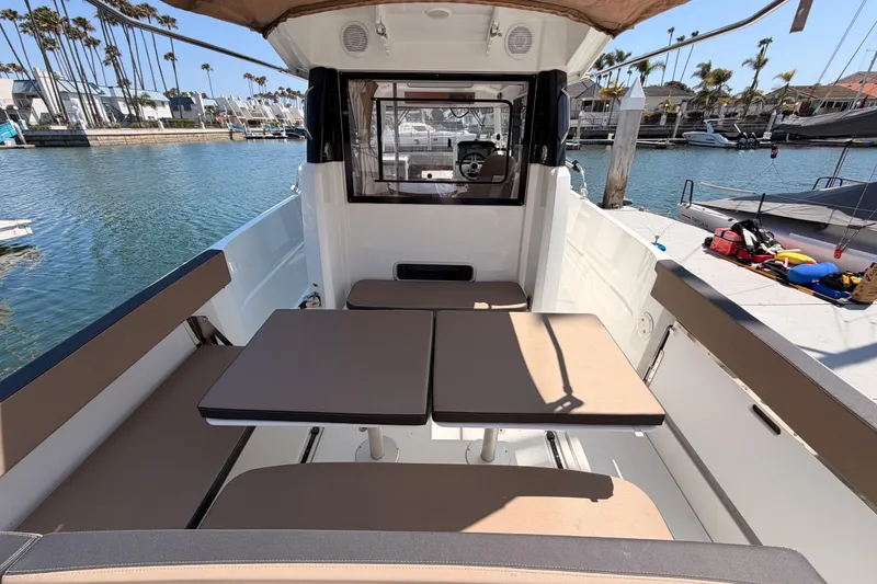 Slide: The Image of 2017 Jeanneau Merry Fisher 855 Marlin boat interior with seating and tables, docked in a marina. - 10