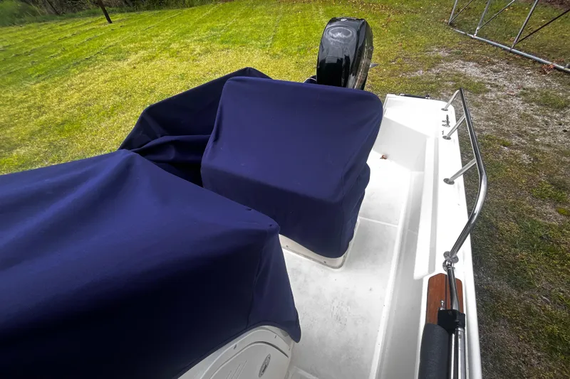 Slide: The Image of 2022 Boston Whaler 150 Montauk boat with blue covers, parked on grass. - 13
