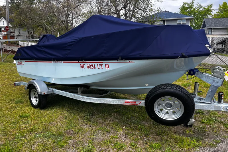 Slide: The Image of 2022 Boston Whaler 150 Montauk boat on trailer, covered with navy tarp, parked on grass. - 14