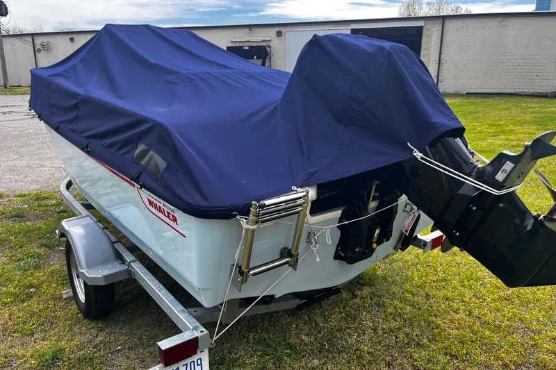 Slide: The Image of 2022 Boston Whaler 150 Montauk boat covered on trailer, parked on grass. - 15