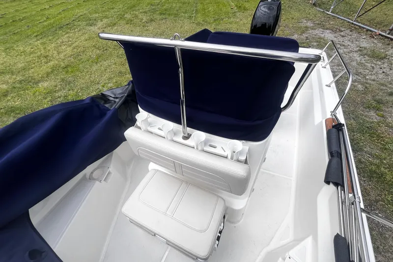 Slide: The Image of 2022 Boston Whaler 150 Montauk interior with seating and storage, on grassy background. - 9