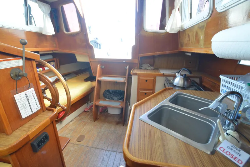 Slide: The Image of 1988 Gulf Pilot House interior with wooden helm, kitchenette, and cozy seating area. - 12