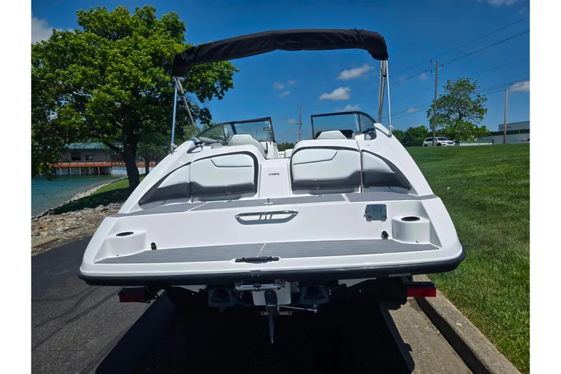 Slide: The Image of 2019 Yamaha Boats SX210 on trailer, rear view, sunny day, near water and greenery. - 2