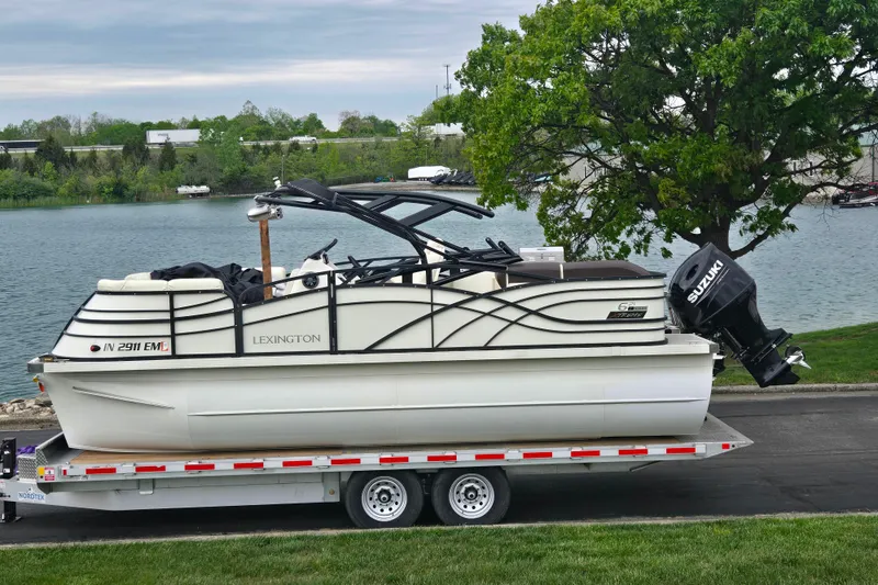 The Image of 2022 Lexington 621TT Extreme pontoon boat on trailer by a lake. - 0