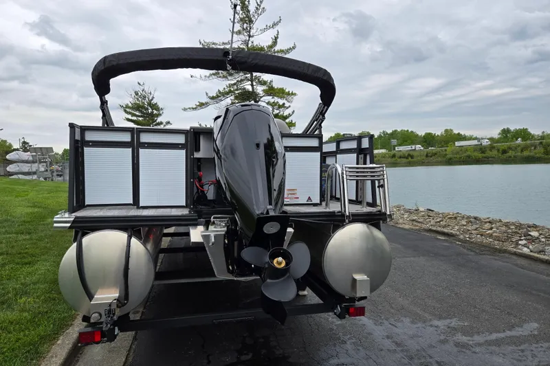 Slide: The Image of 2024 Qwest Angler Qwest XRE pontoon boat by a lakeside, showcasing rear motor and pontoons. - 2