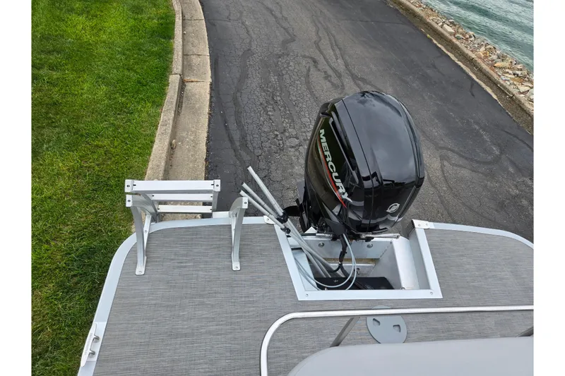 Slide: The Image of 2023 Bennington 22 LSB boat with Mercury outboard motor, docked by a lakeside road. - 17