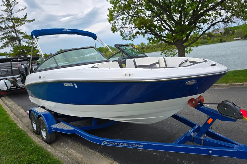 Slide: The Image of 2020 Monterey M-20 boat on trailer by lakeside, featuring sleek blue and white design. - 8