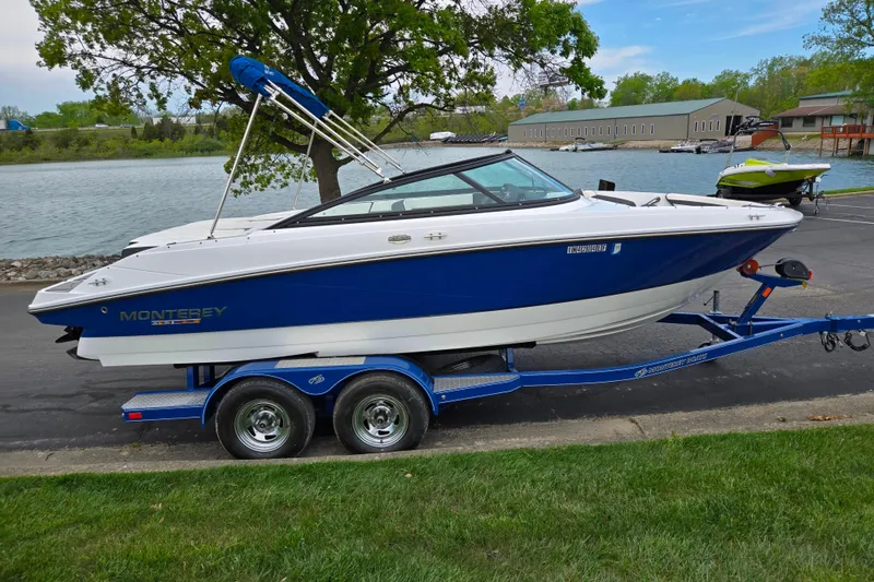 Slide: The Image of 2020 Monterey M-20 boat on trailer by a lakeside, featuring sleek blue and white design. - 9