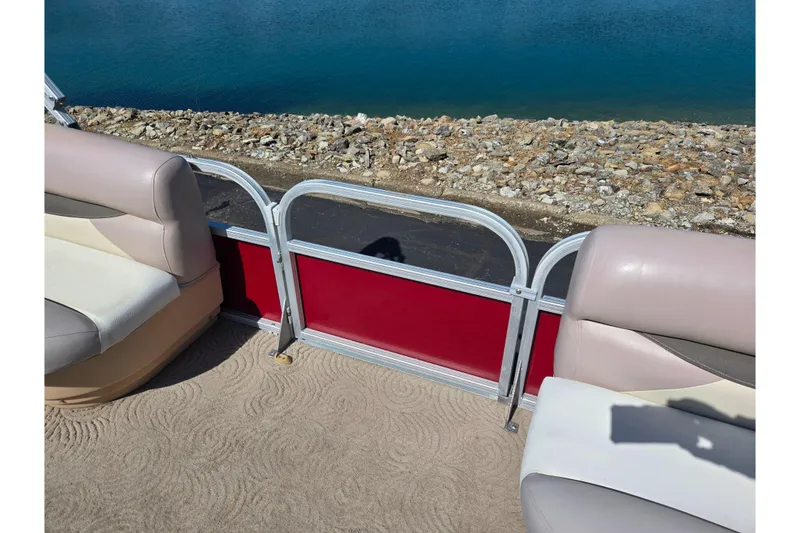 Slide: The Image of 2014 Sun Tracker Party Barge 20 DLX interior with beige seating and red paneling by water. - 15
