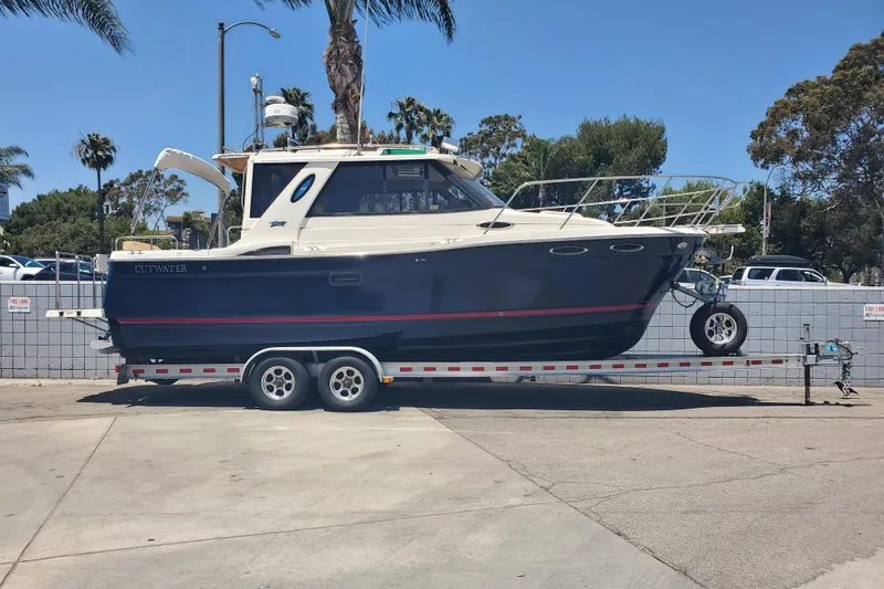 The Image of 2013 Cutwater 26 boat on trailer, parked outdoors under clear blue sky. - 0
