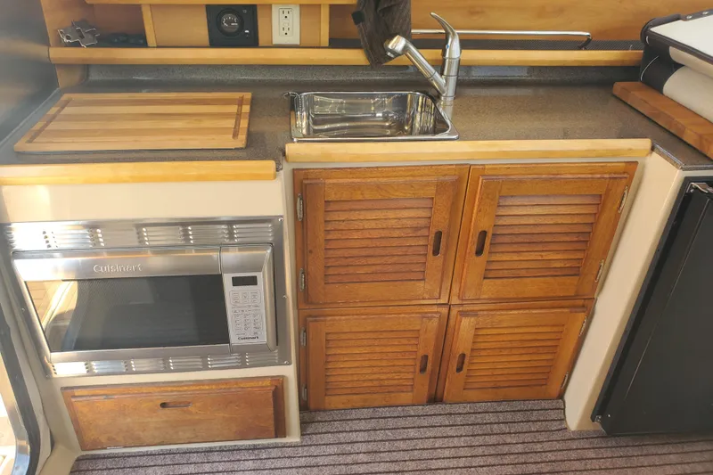 Slide: The Image of 2013 Cutwater 26 boat kitchen with wooden cabinets, microwave, sink, and cutting board. - 10