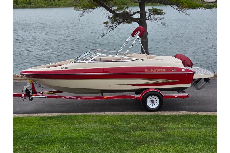 The Image of 2005 Glastron GX 205 boat on trailer by a lake, featuring red and beige design. - 0