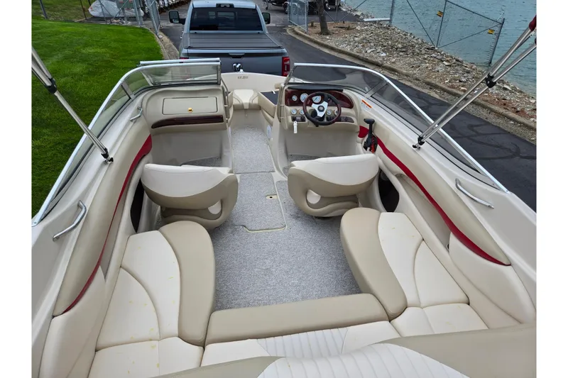 Slide: The Image of 2005 Glastron GX 205 boat interior with beige seating and red accents near a lake. - 10