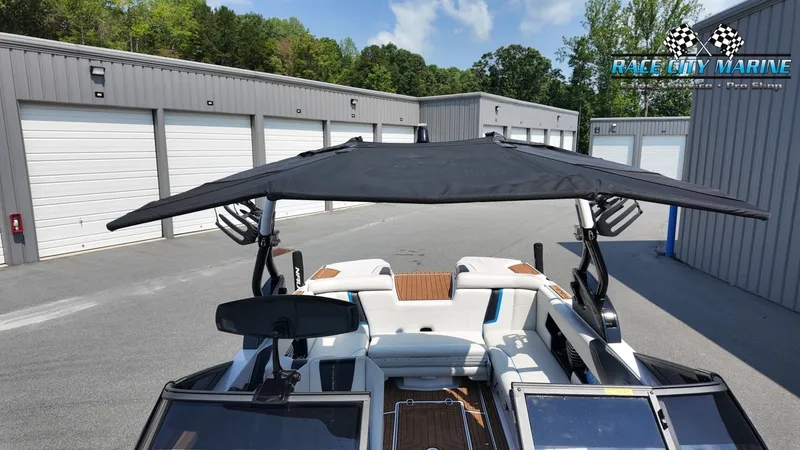 Slide: The Image of A 2015 Nautique G23 boat with a black sunshade, parked in front of garages. White seats are visible. - 31