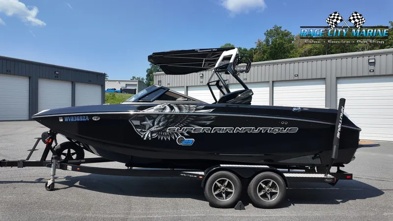 Slide: The Image of 2015 Nautique G23 on a trailer, black with graphics, parked in front of a building. - 2