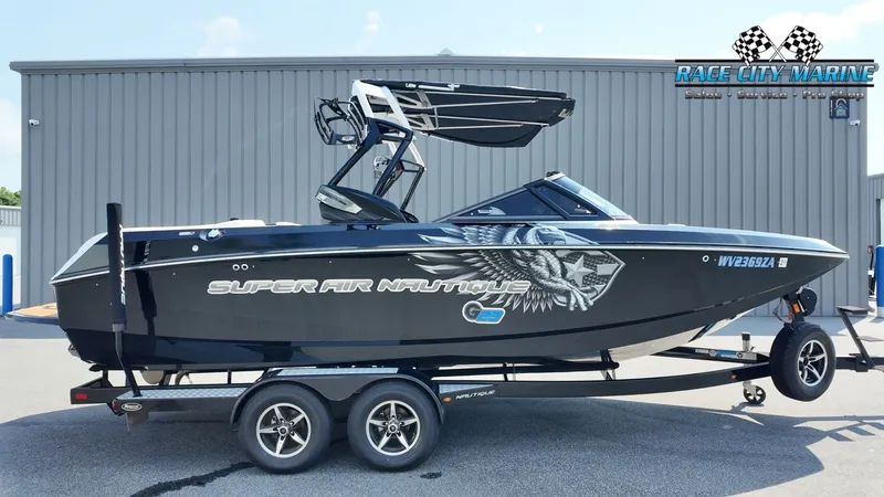 The Image of A black 2015 Nautique G23 boat on a trailer in front of a gray building. - 1