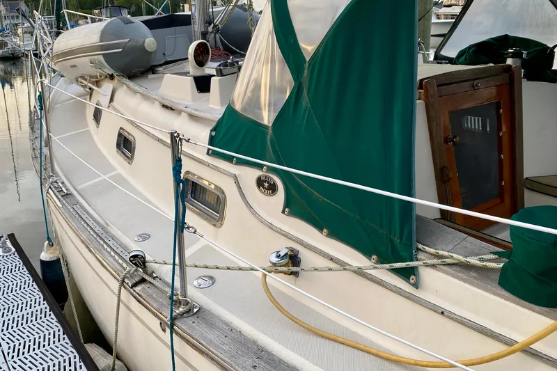 Slide: The Image of 1992 Island Packet 29 sailboat docked, featuring green canvas covers and a wooden cabin door. - 21