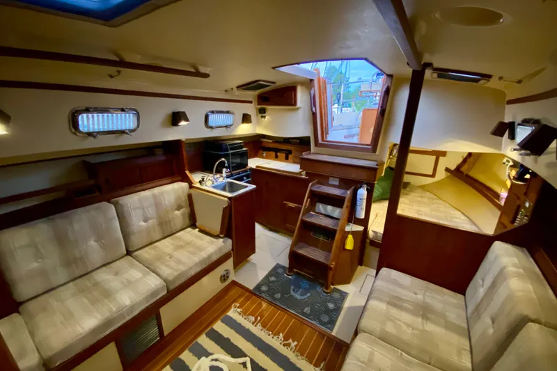 Slide: The Image of Interior of a 1992 Island Packet 29 sailboat, featuring cozy seating and a compact kitchen. - 48