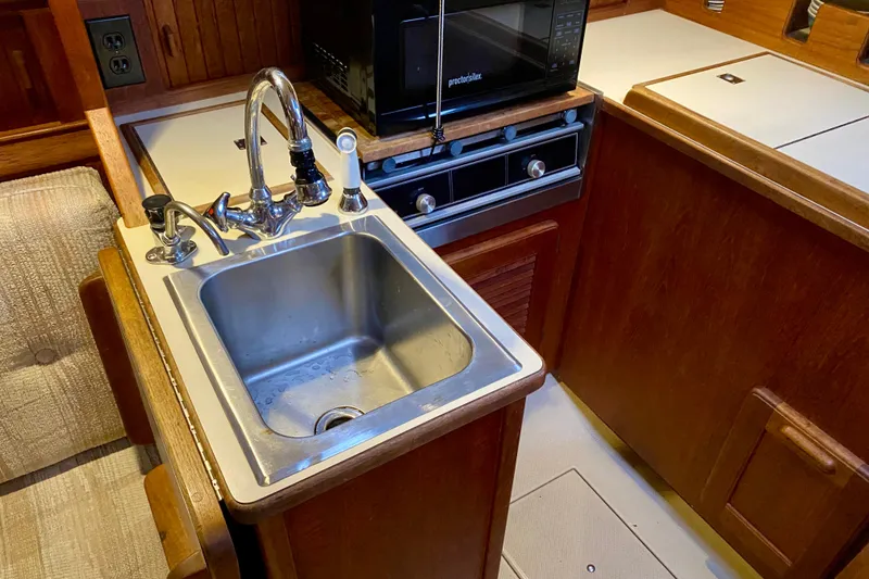 Slide: The Image of Compact kitchen area in a 1992 Island Packet 29 sailboat, featuring a sink and stove. - 49