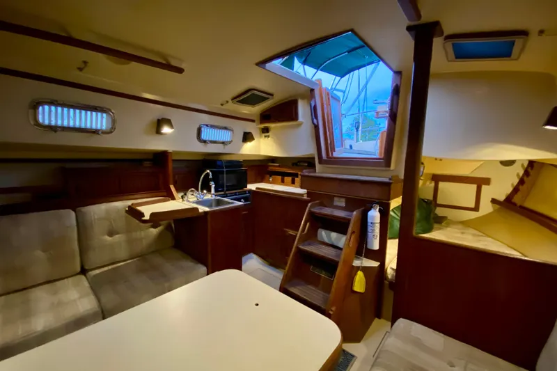 Slide: The Image of Interior of a 1992 Island Packet 29 sailboat, featuring cozy seating and a compact kitchen area. - 65