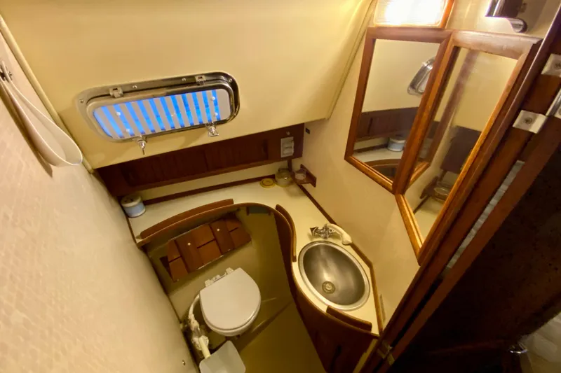Slide: The Image of 1992 Island Packet 29 yacht bathroom with sink, toilet, mirror, and porthole window. - 75