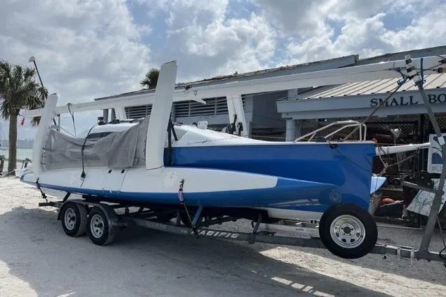 Slide: The Image of 1996 Farrier F-25C trimaran on trailer near small boat shop, under cloudy sky. - 4