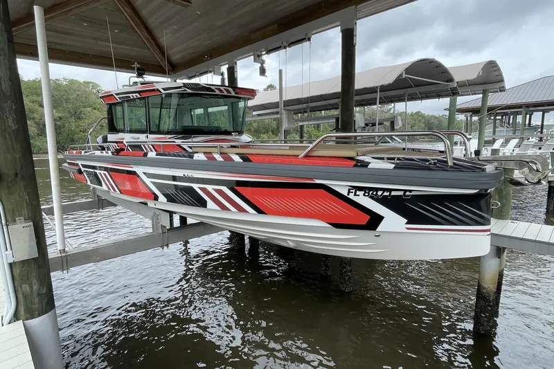 The Image of 2021 Axopar 28 Cabin boat with striking red and black design, docked under a shelter. - 0