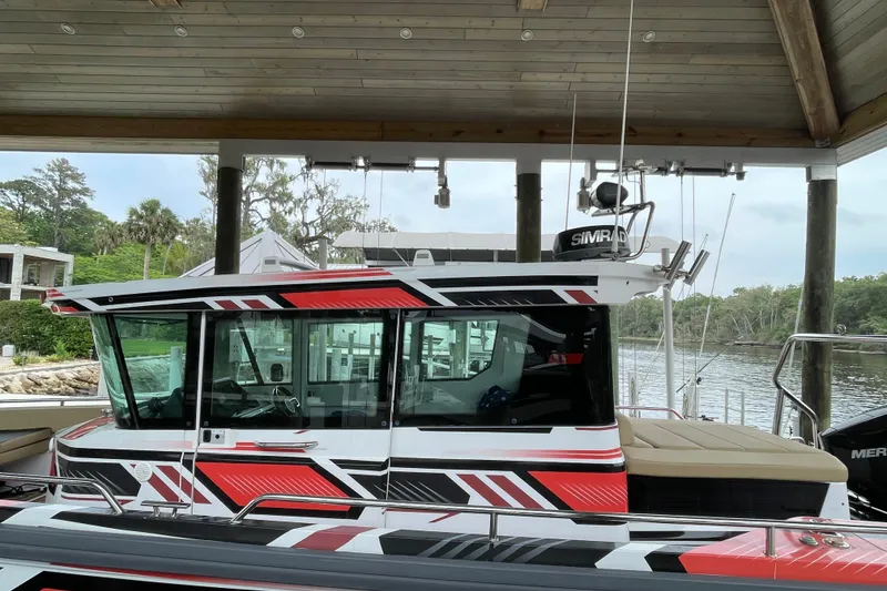 Slide: The Image of 2021 Axopar 28 Cabin boat with striking red and black design, docked under a wooden roof. - 3