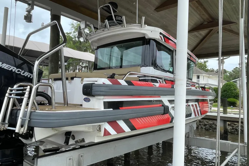 Slide: The Image of 2021 Axopar 28 Cabin boat with vibrant red and black design, docked under a shelter. - 7
