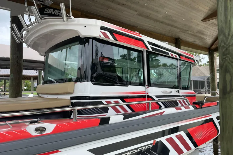 Slide: The Image of 2021 Axopar 28 Cabin boat with striking red and black graphics docked under a wooden roof. - 8