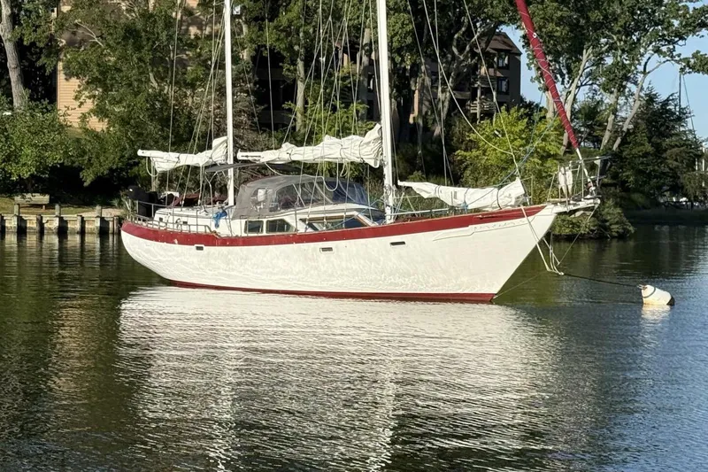 The Image of Vintage 1979 Hardin 44 sailboat anchored on a calm lake, surrounded by trees. - 1