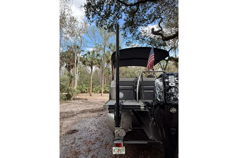 Slide: The Image of 2023 Barletta Corsa 23U pontoon boat with American flag, parked in wooded area. - 10