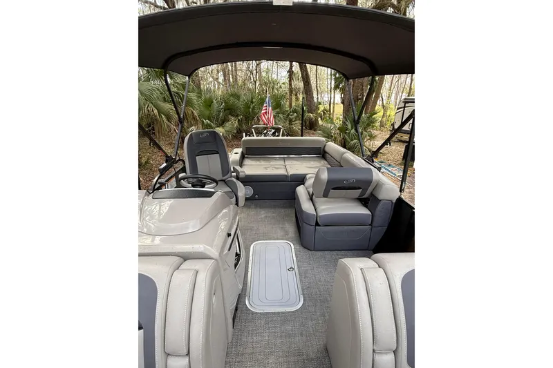 Slide: The Image of 2023 Barletta Corsa 23U pontoon boat interior with seating and helm, surrounded by trees. - 4