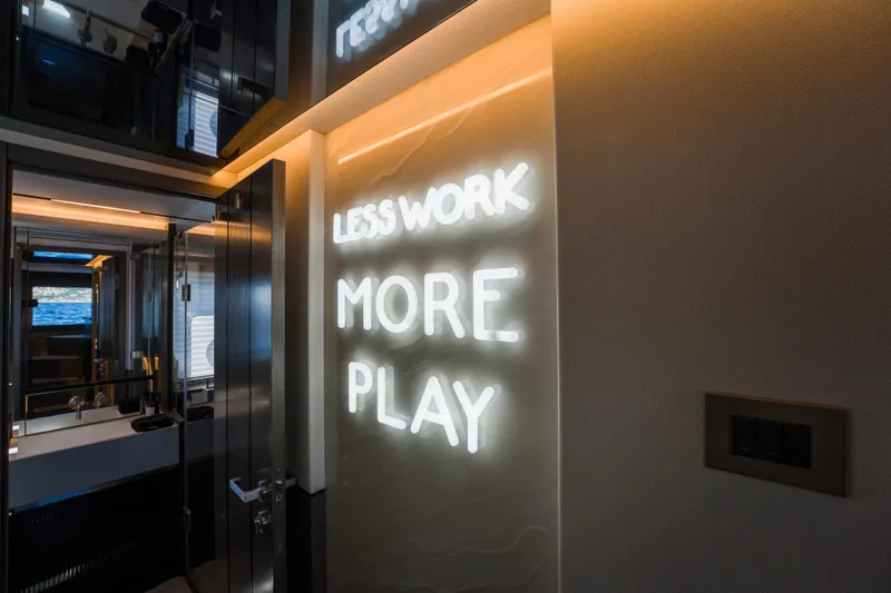 Slide: The Image of Illuminated "Less Work More Play" sign inside 2024 Pearl 72 yacht interior. - 78