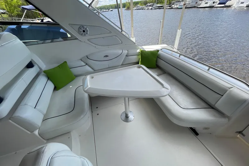 Slide: The Image of 1997 Bayliner 4085 Avanti boat interior with white seating, green cushions, and a table by the water. - 9