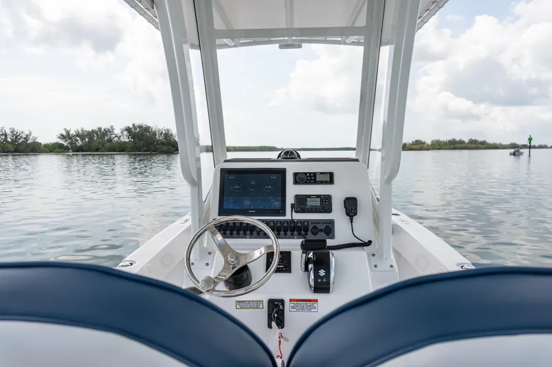 Slide: The Image of 2026 Twin Vee 22 BayCat boat dashboard with steering wheel and navigation controls on calm water. - 13
