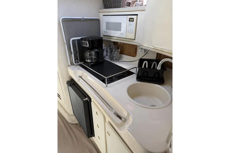 Slide: The Image of Compact kitchen area in a 1997 Sea Ray 290 Sundancer boat, featuring a sink, stove, and microwave. - 18