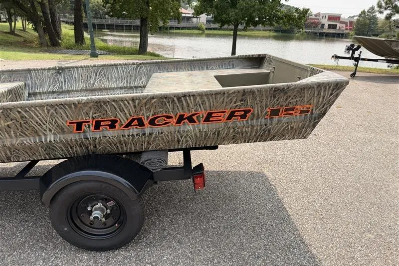 Slide: The Image of 2026 Tracker Grizzly 15 Jon boat with camouflage design on a trailer by a lake. - 10