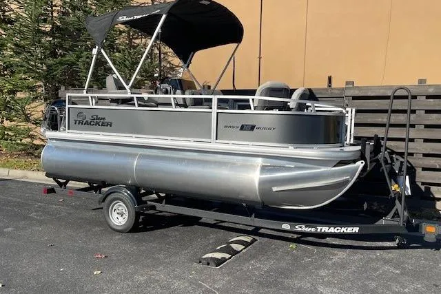 The Image of 2026 Sun Tracker Bass Buggy 16 XL Select pontoon boat on trailer, parked outdoors. - 0