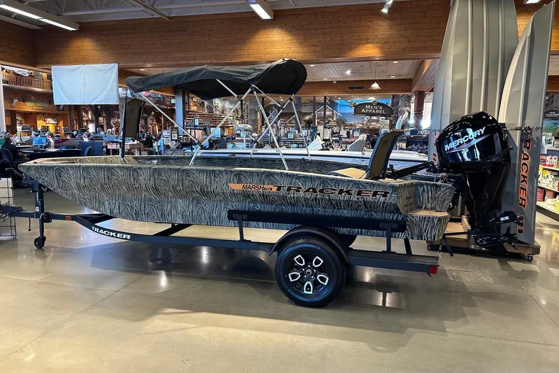 Slide: The Image of 2026 Tracker Grizzly 1756 T Marsh boat displayed indoors with Mercury outboard motor. - 2