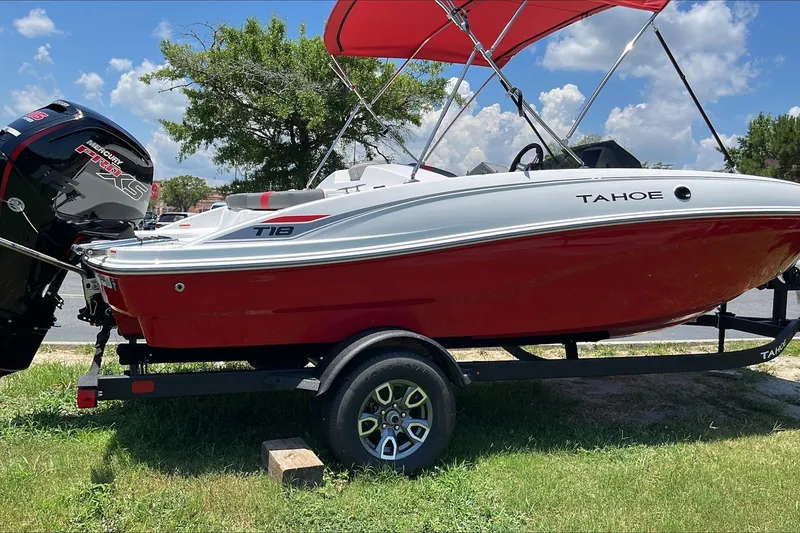 Slide: The Image of 2026 Tahoe T18 boat with red hull and canopy on trailer, parked on grass. - 2