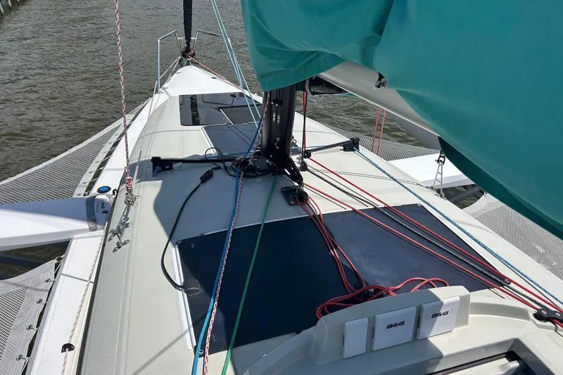 Slide: The Image of 2023 Corsair 880 sailboat deck with rigging and netting on the water. - 14