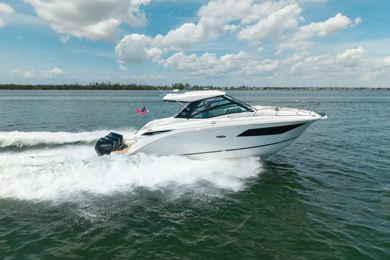 The Image of 2024 Sea Ray Sundancer 320 Outboard cruising on open water under a clear blue sky. - 0